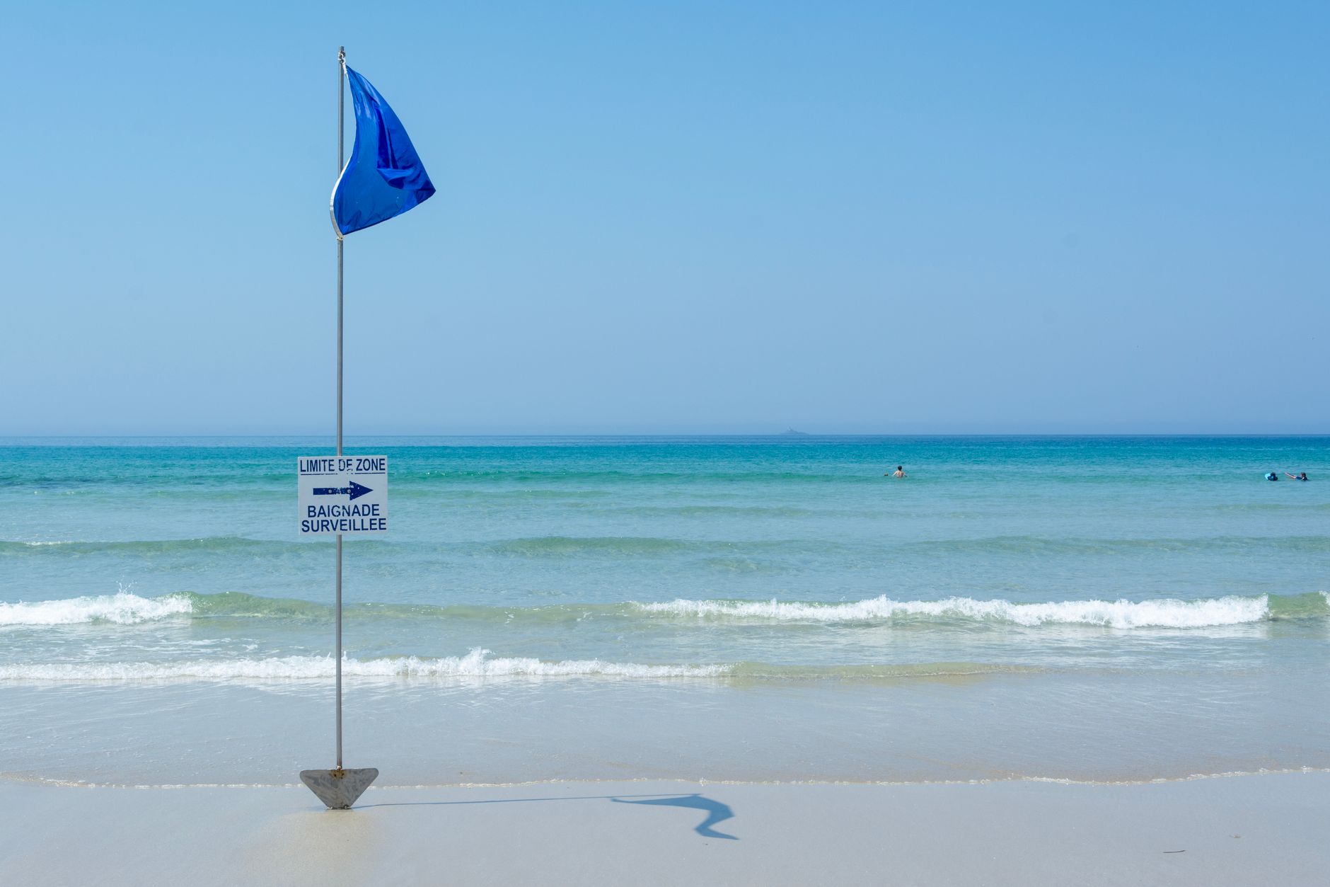 Tranquil beach with a blue flag and safety sign, perfect for summer travel.