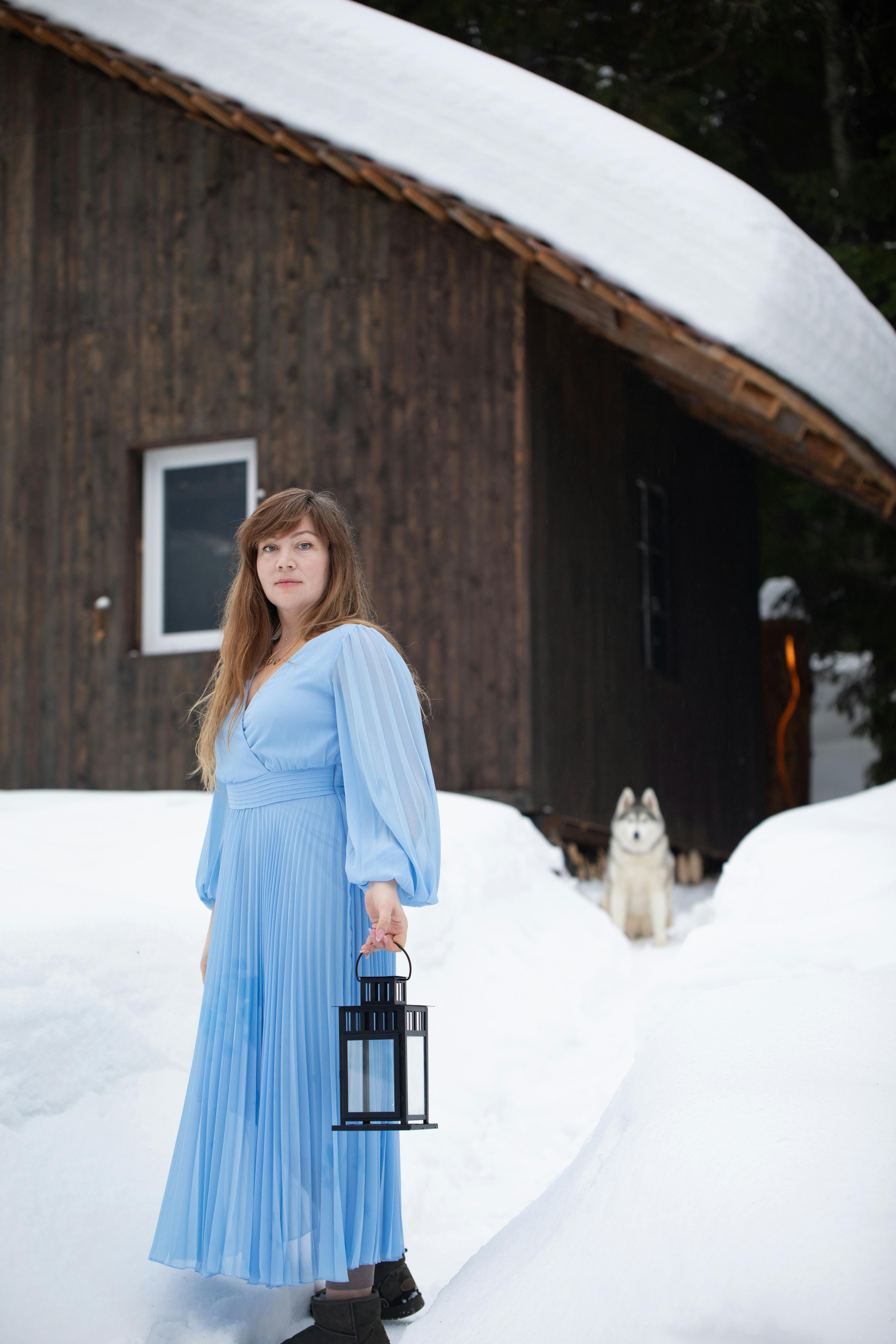 woman in blue maxi dress holding hand lamp on snow path