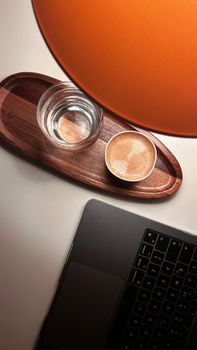 Top view of a wooden tray with espresso and water next to a laptop.