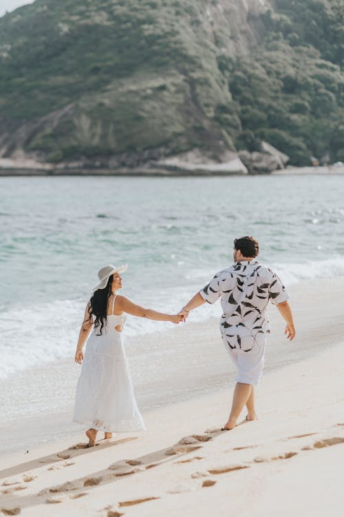A Couple Holding Hands and Walking on a Beach 