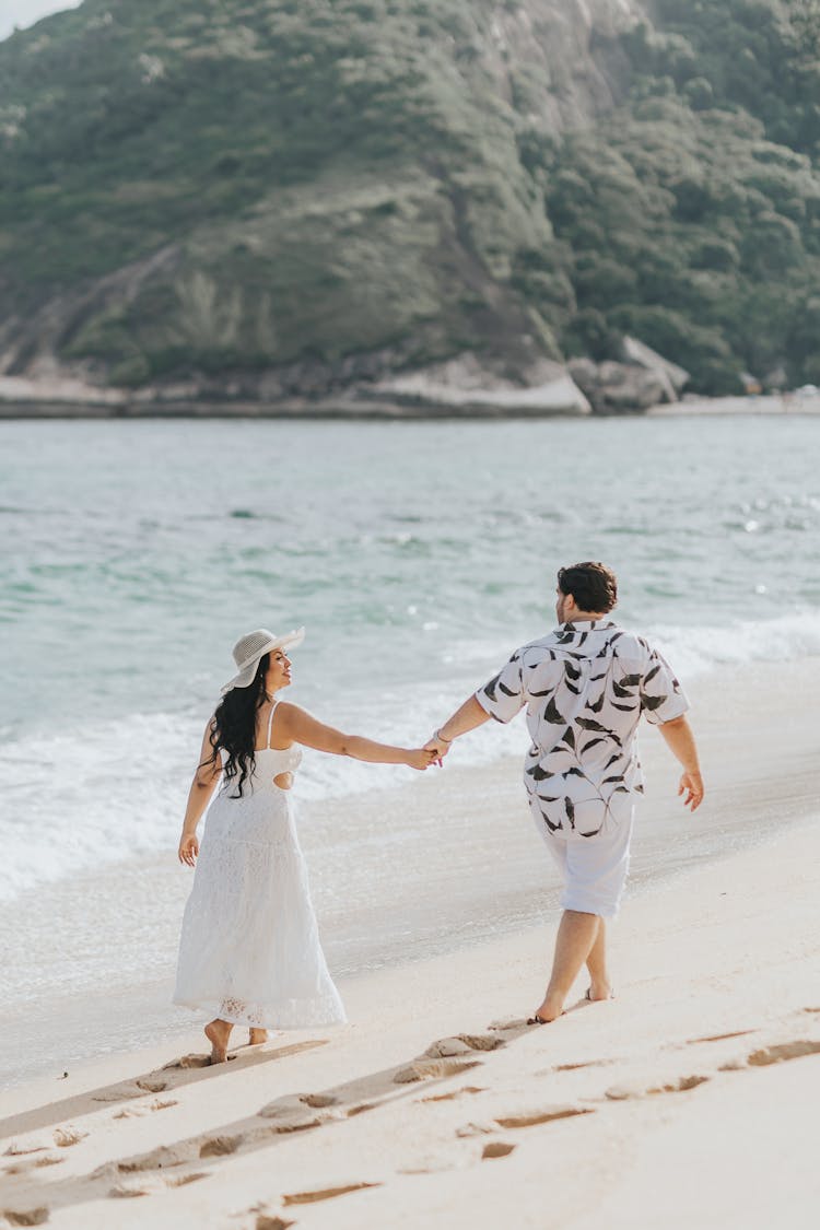 A Couple Holding Hands And Walking On A Beach 