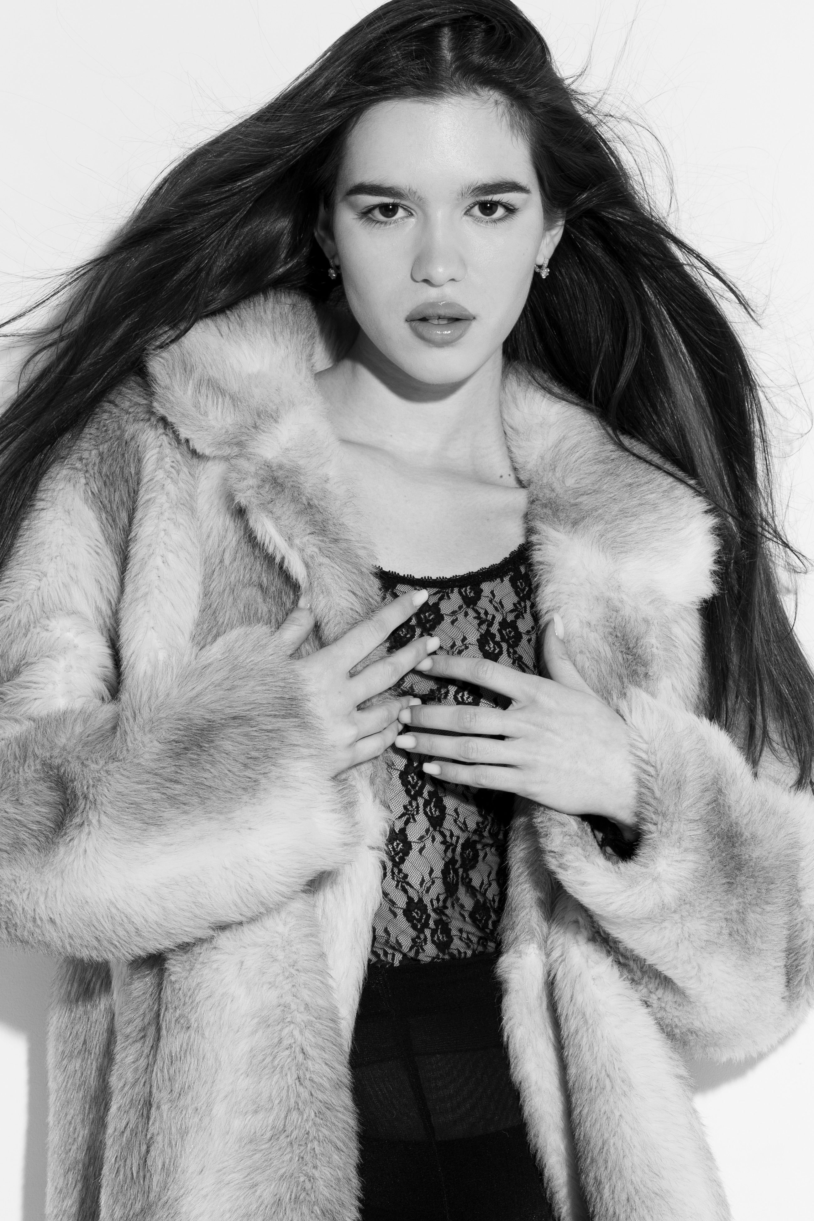 Black and white portrait of a woman in a luxurious fur coat posing confidently.