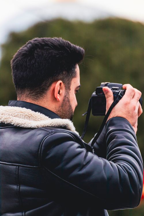 Free Side view of a man with a camera photographing outdoors in a leather jacket. Stock Photo