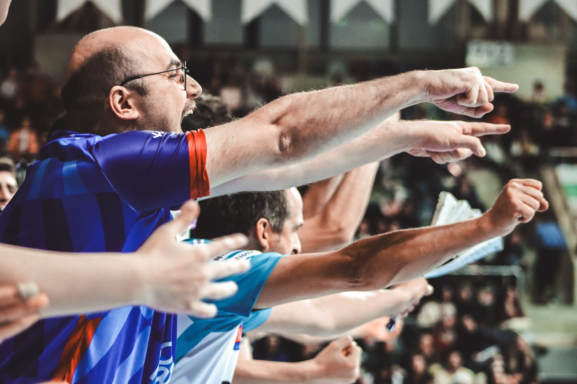 Energized sports fans pointing and cheering during a thrilling match in a stadium.