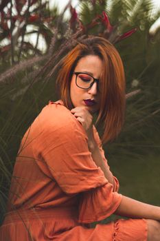 在郁郁葱葱的公园里，一位红发女子优雅地站在充满活力的植物旁