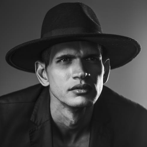 A man in a hat and jacket is posing for a black and white photo