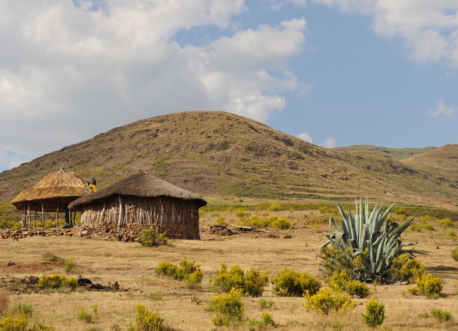 Scenic view of traditional huts in a dry, mountainous African landscape under a blue sky.