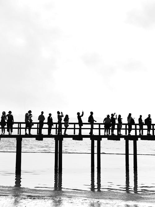 A black and white photo of people standing on a pier
