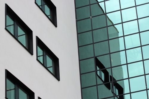 Free Close-up of a modern building facade with glass windows reflecting the urban environment. Stock Photo