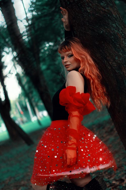 A woman with red hair posing in front of a tree