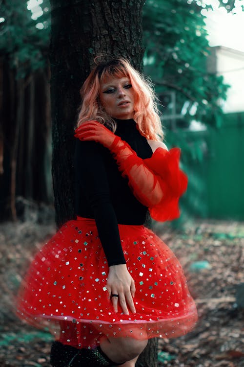 A woman in a red skirt posing near a tree