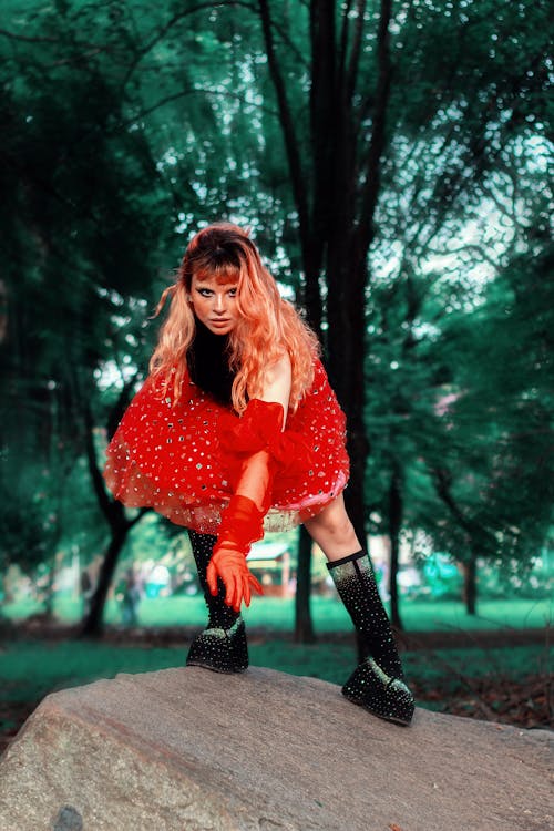 A girl in a red dress and gloves is standing on a rock