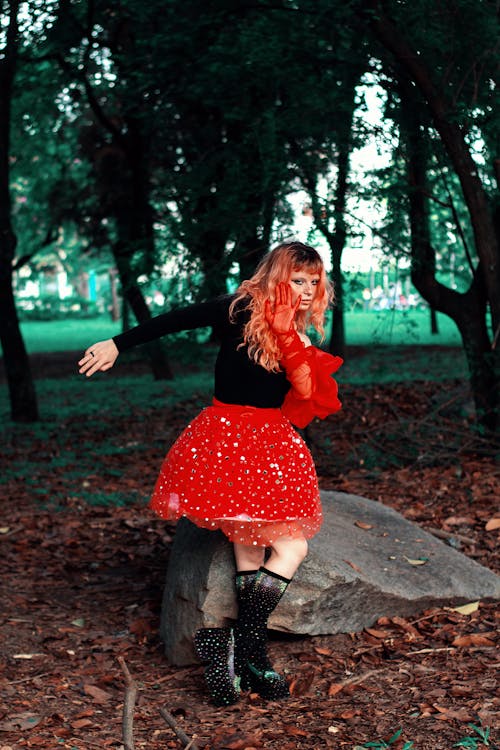 A woman in a red skirt and black boots is standing in the woods