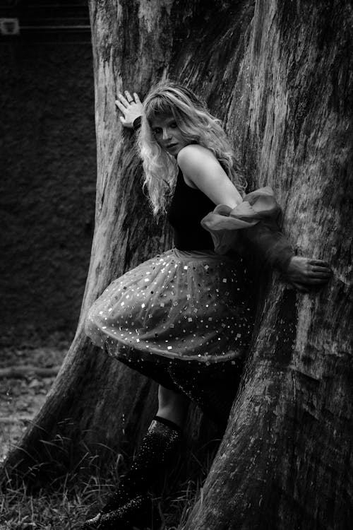 A woman in a skirt leaning against a tree