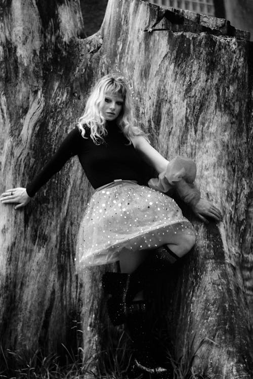 A woman in a skirt and boots sitting on a tree stump