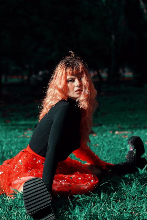 A woman in a red skirt and black boots sitting in the grass