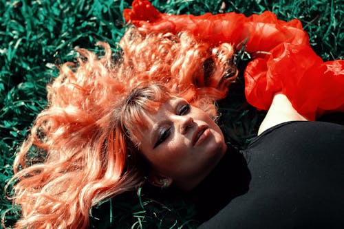 A woman laying on the grass with her hair dyed red