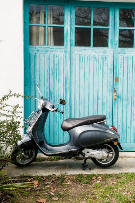 A classic Vespa scooter parked in front of a weathered turquoise wooden door. Perfect blend of vintage style and vibrant color.