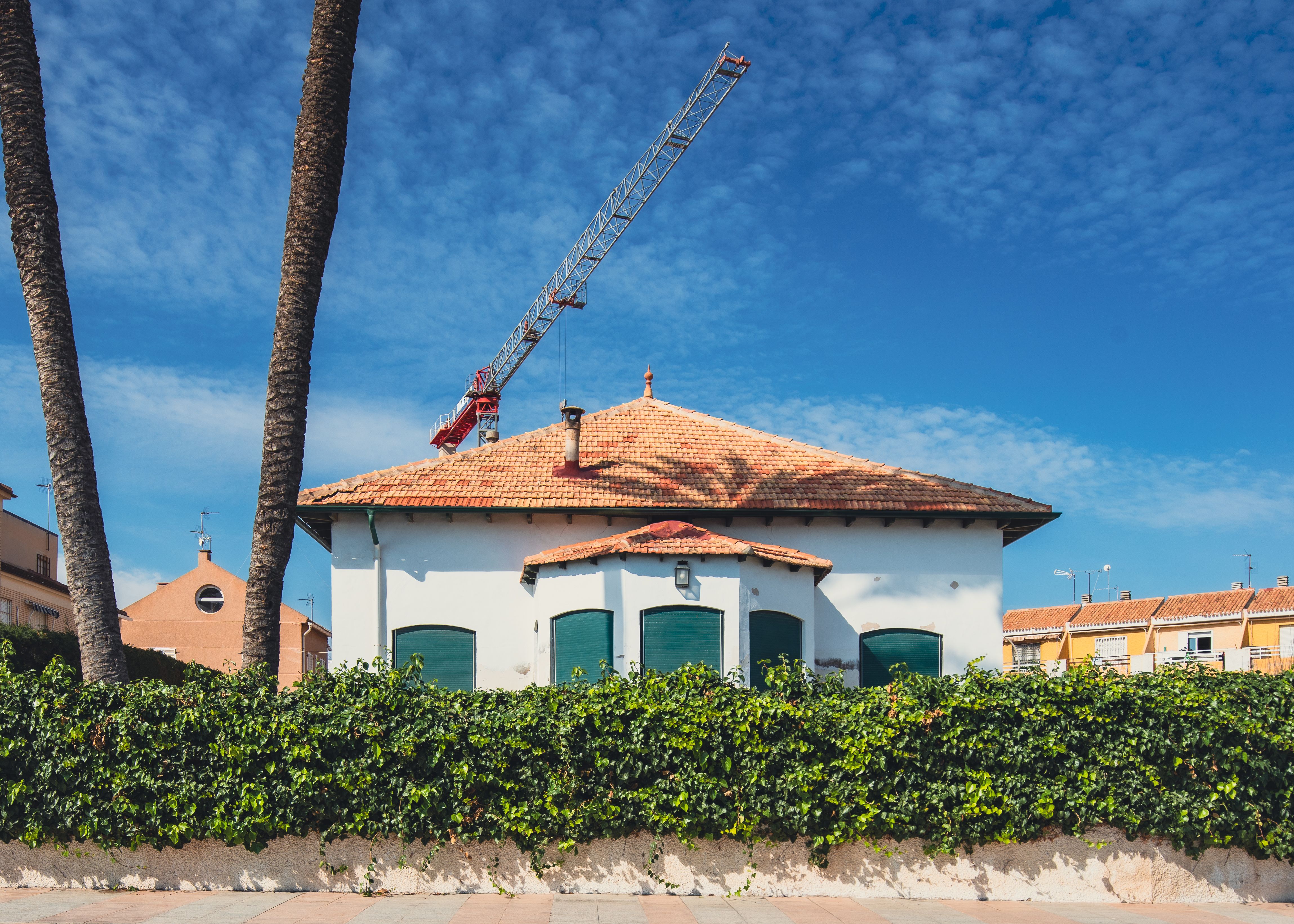 Beautiful house in San Javier, Spain, featuring a construction crane and palm trees under a clear blue sky.