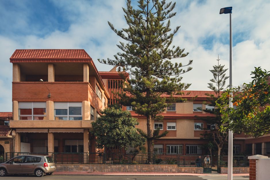 Una vista soleada de una calle con un edificio residencial de techo naranja y árboles en San Javier, España.