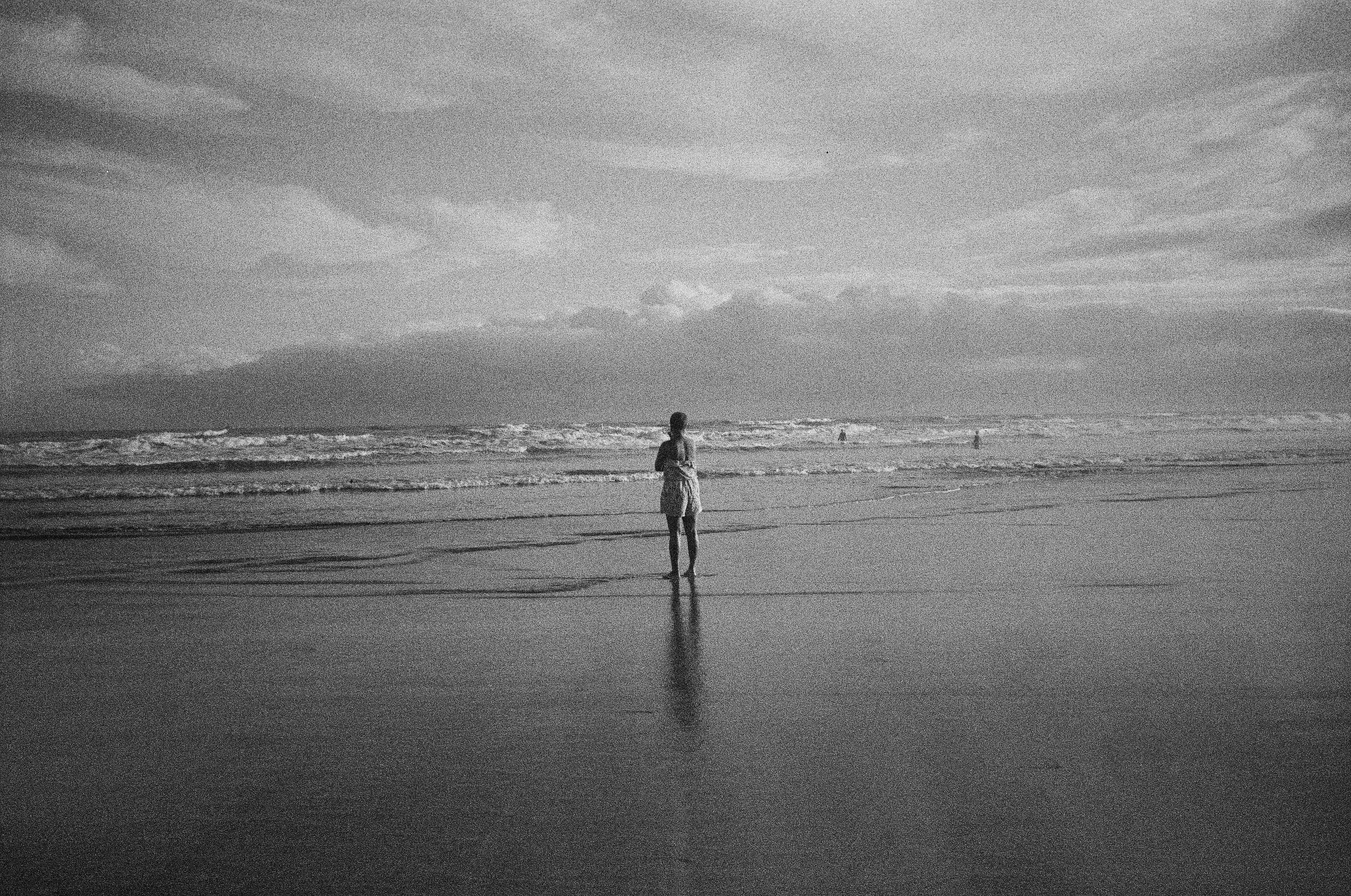 A person stands alone on a tranquil beach, reflecting in the serene waves.