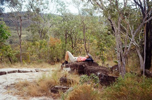Free Woman lying on a rock surrounded by a peaceful forest landscape, enjoying nature. Stock Photo