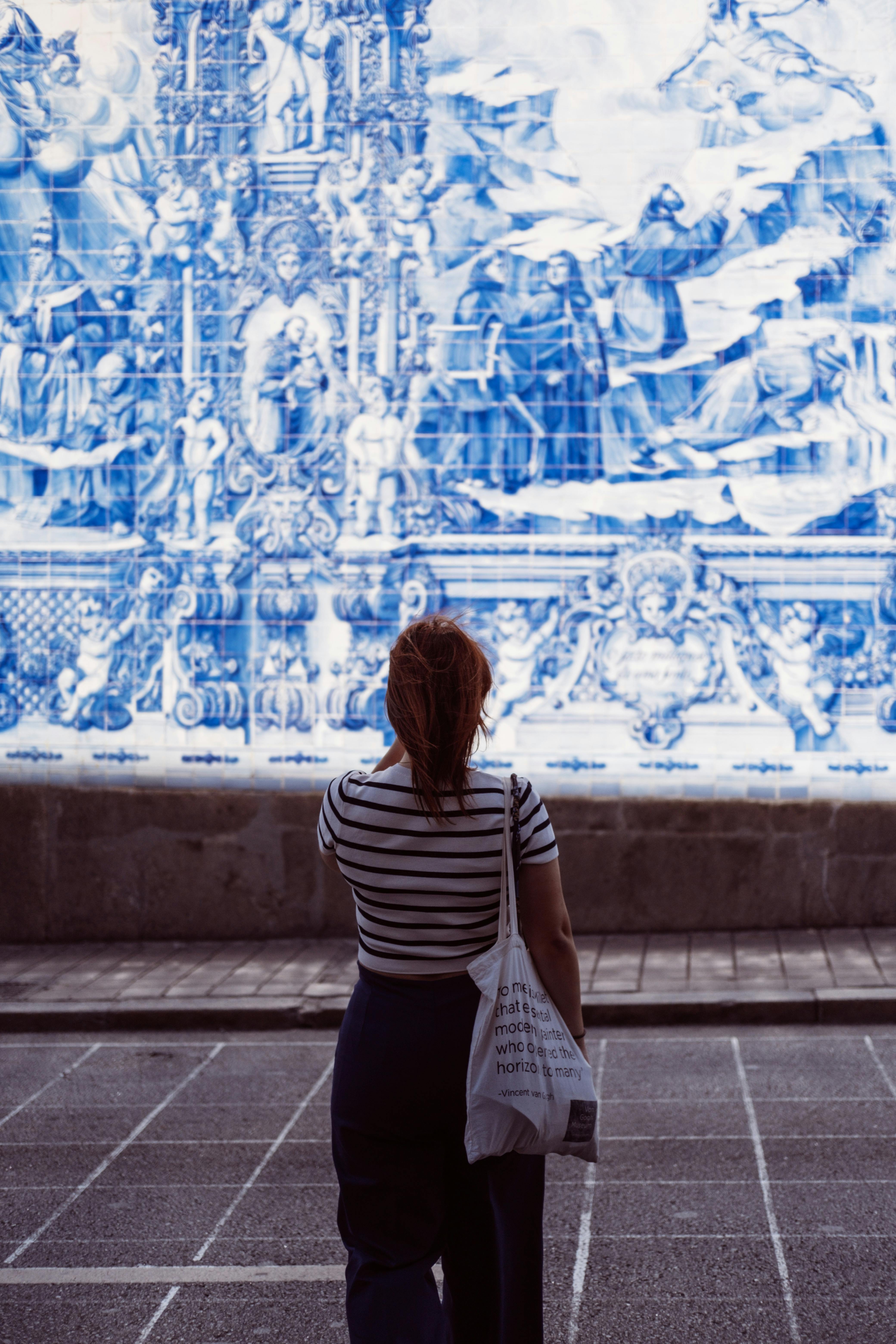 A woman stands in front of intricate azulejo tile art in Porto, Portugal.