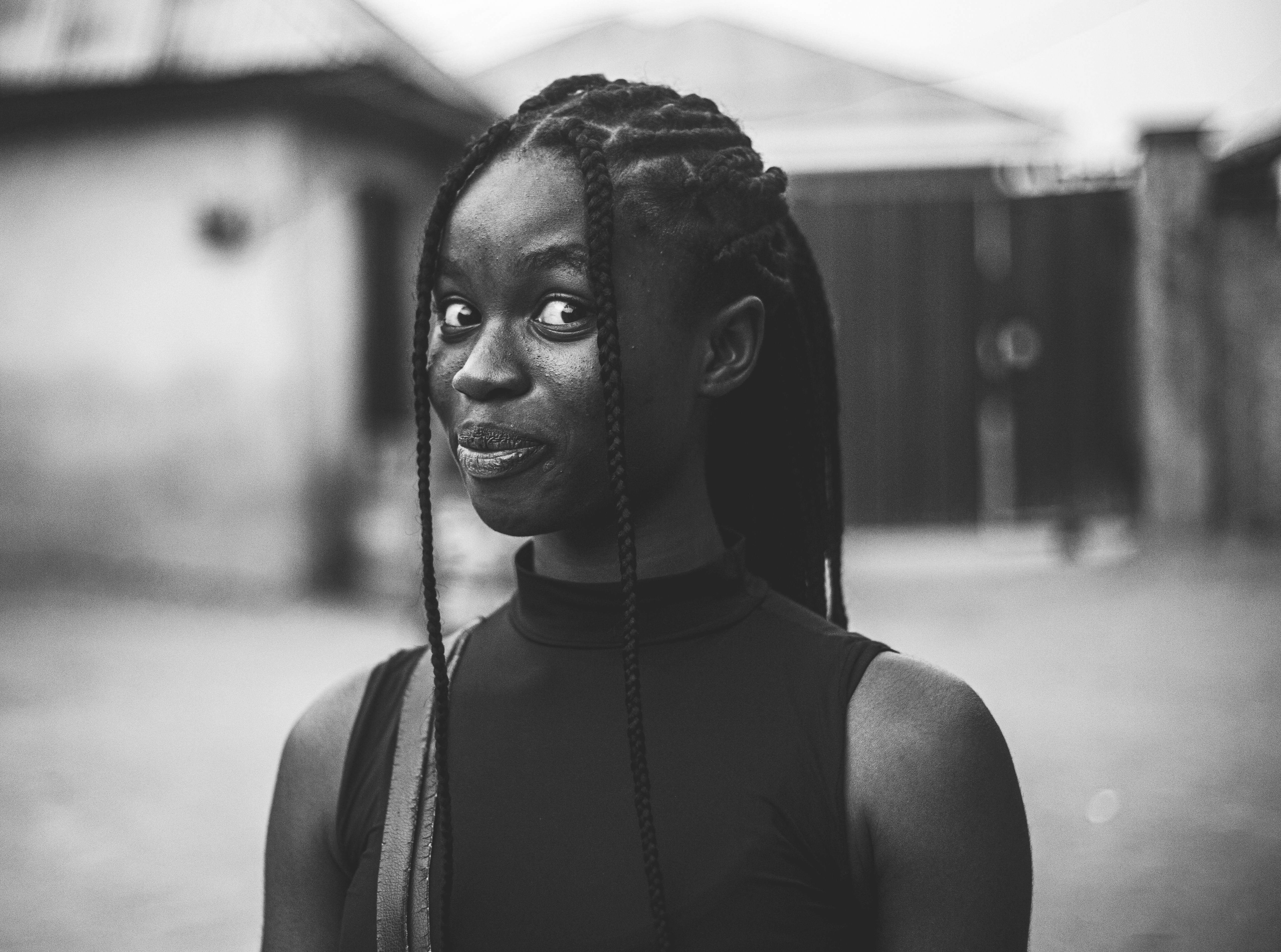 Black and white portrait of a young woman with braids, expressing playfulness in Abuja, Nigeria.