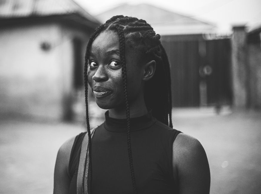 Black and white portrait of a young woman with braids, expressing playfulness in Abuja, Nigeria.