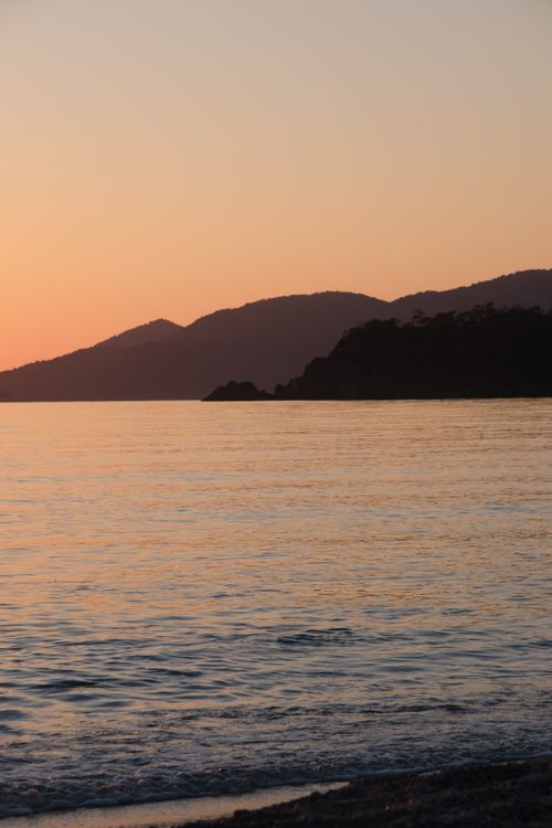 Free Peaceful sunset view over the ocean with silhouetted mountains and calm waters. Stock Photo