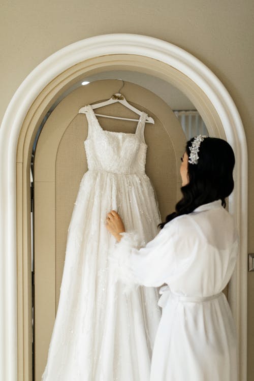 A bride in a white robe looking at her wedding dress