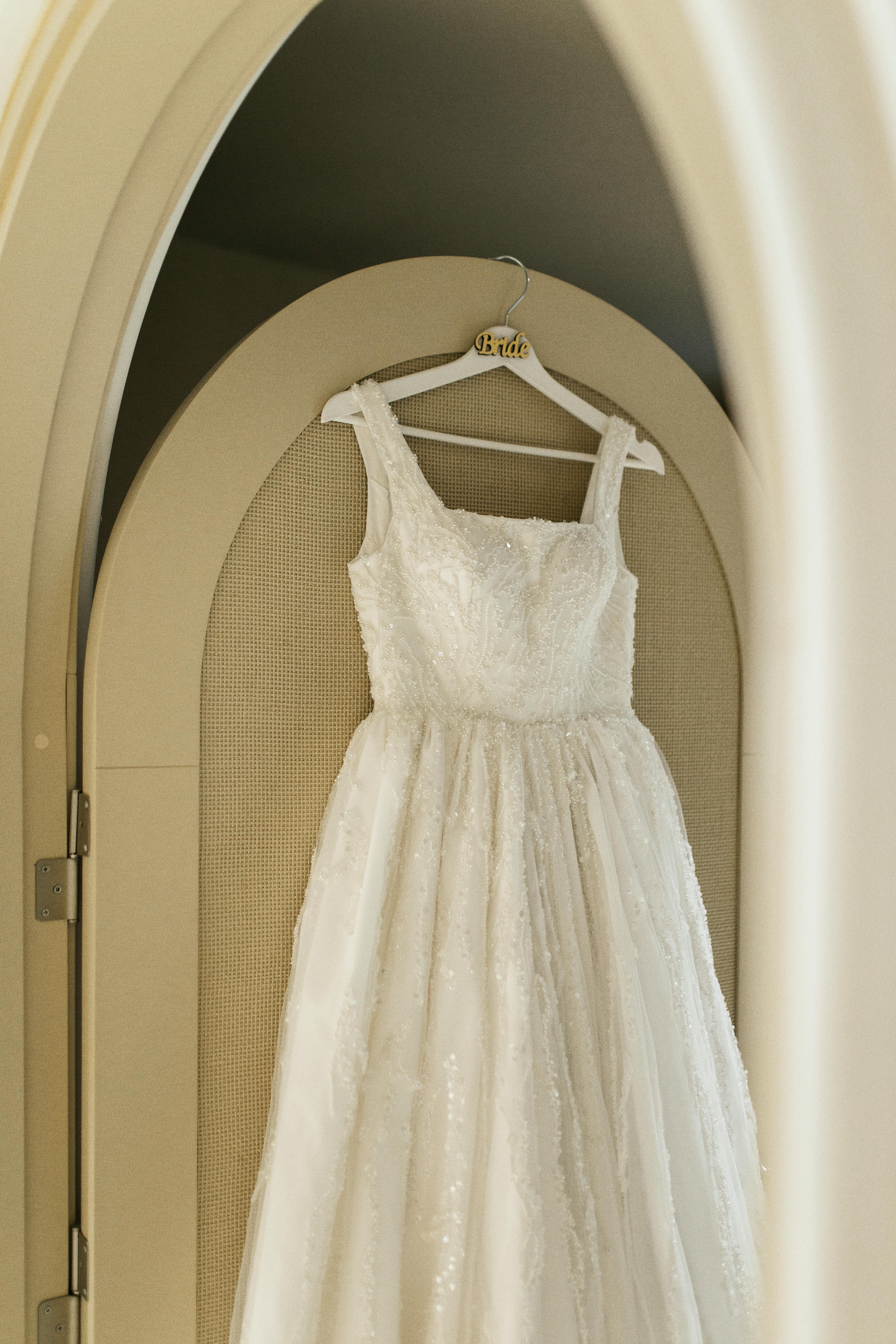 A beautifully detailed wedding dress hanging on an arched door frame, perfect for bridal fashion.