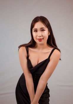 Stylish studio portrait of a young Asian woman in an elegant black dress, posing with a smile.