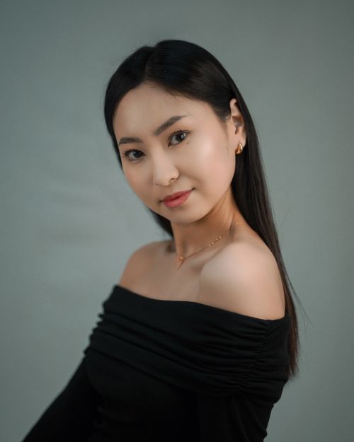 Free Sophisticated studio portrait of an Asian woman wearing an off-shoulder black dress with a gentle smile. Stock Photo
