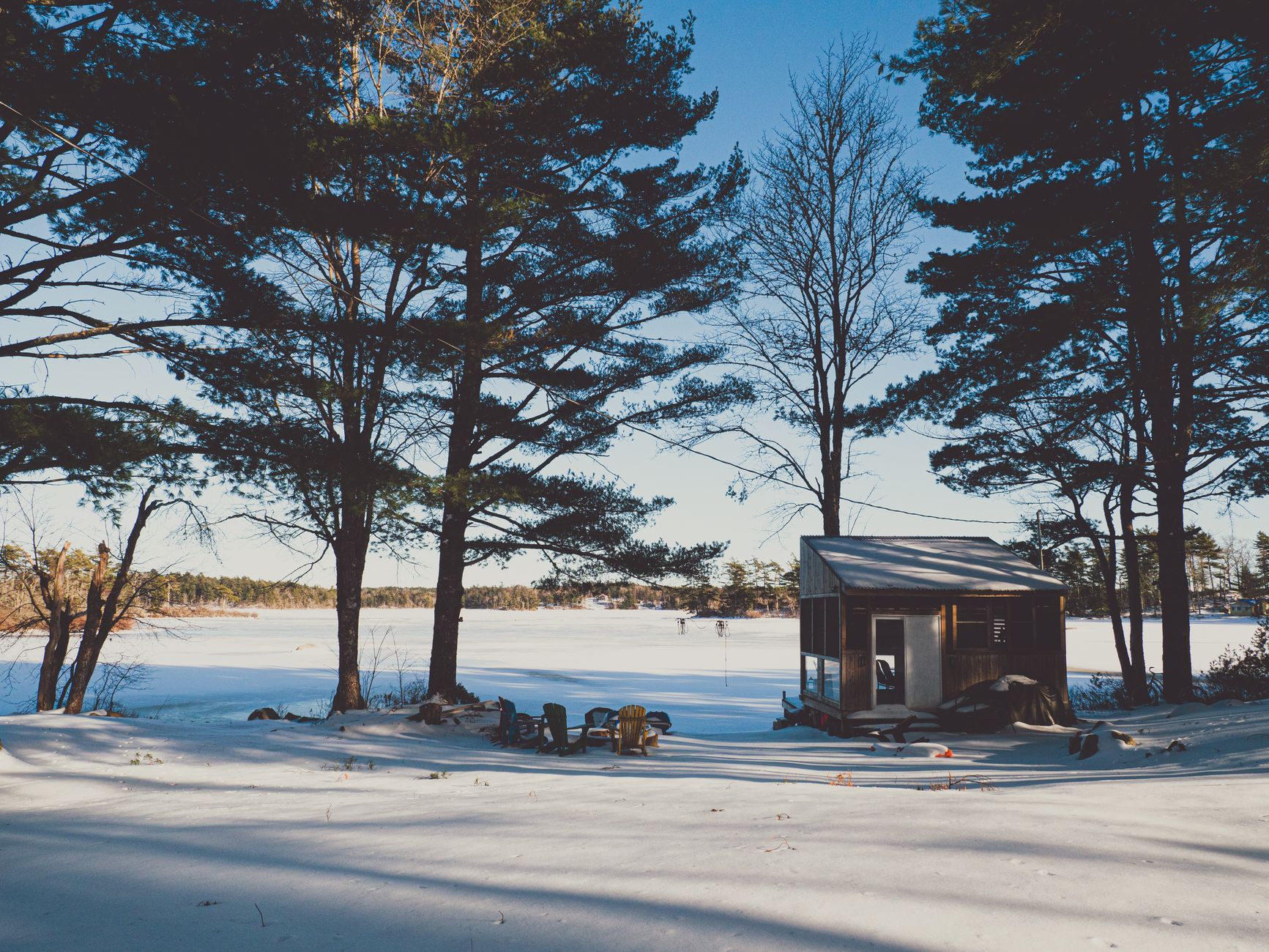 a cedar shake cottage on a wooded lake lot with a stone fire pit and two kayaks by the water