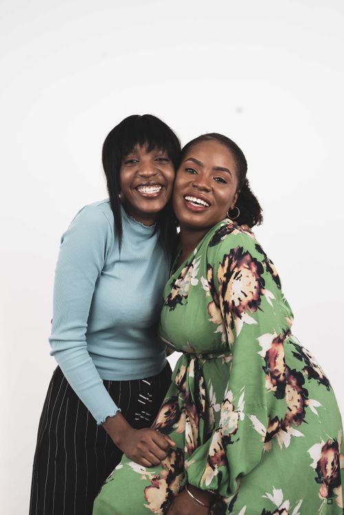 Free Two women in vibrant attire share a joyful hug against a plain backdrop. Stock Photo