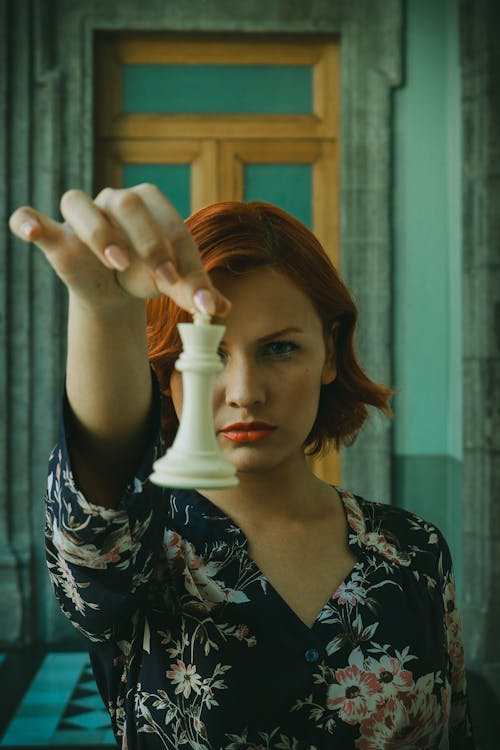 Redhead Woman Holding Out White Chess Piece in front of Her