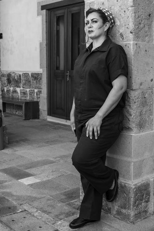 A woman in a black shirt and pants leaning against a wall