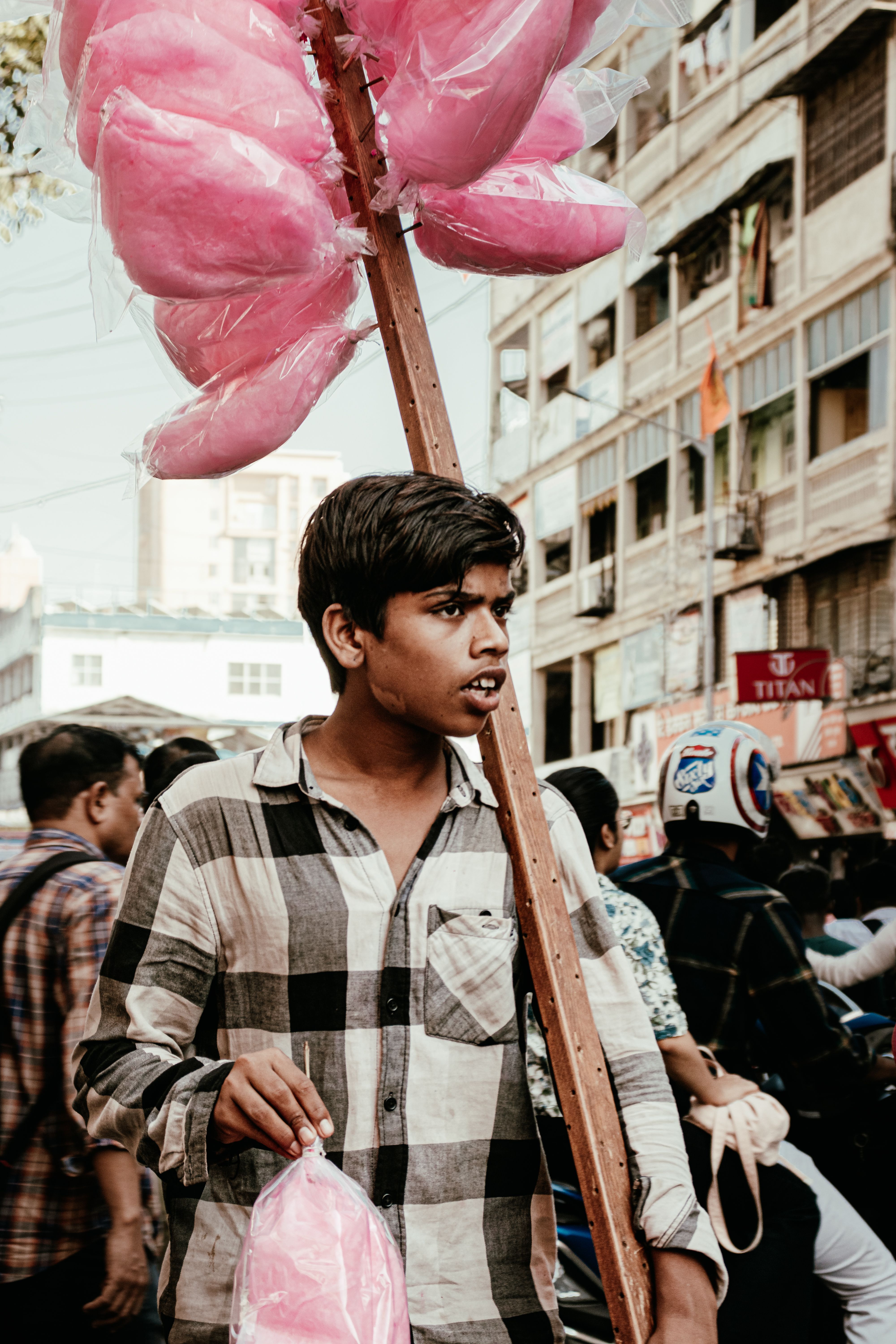 Teen boy holding pink cotton candy in bustling Mumbai street scene, showcasing urban vibrancy.