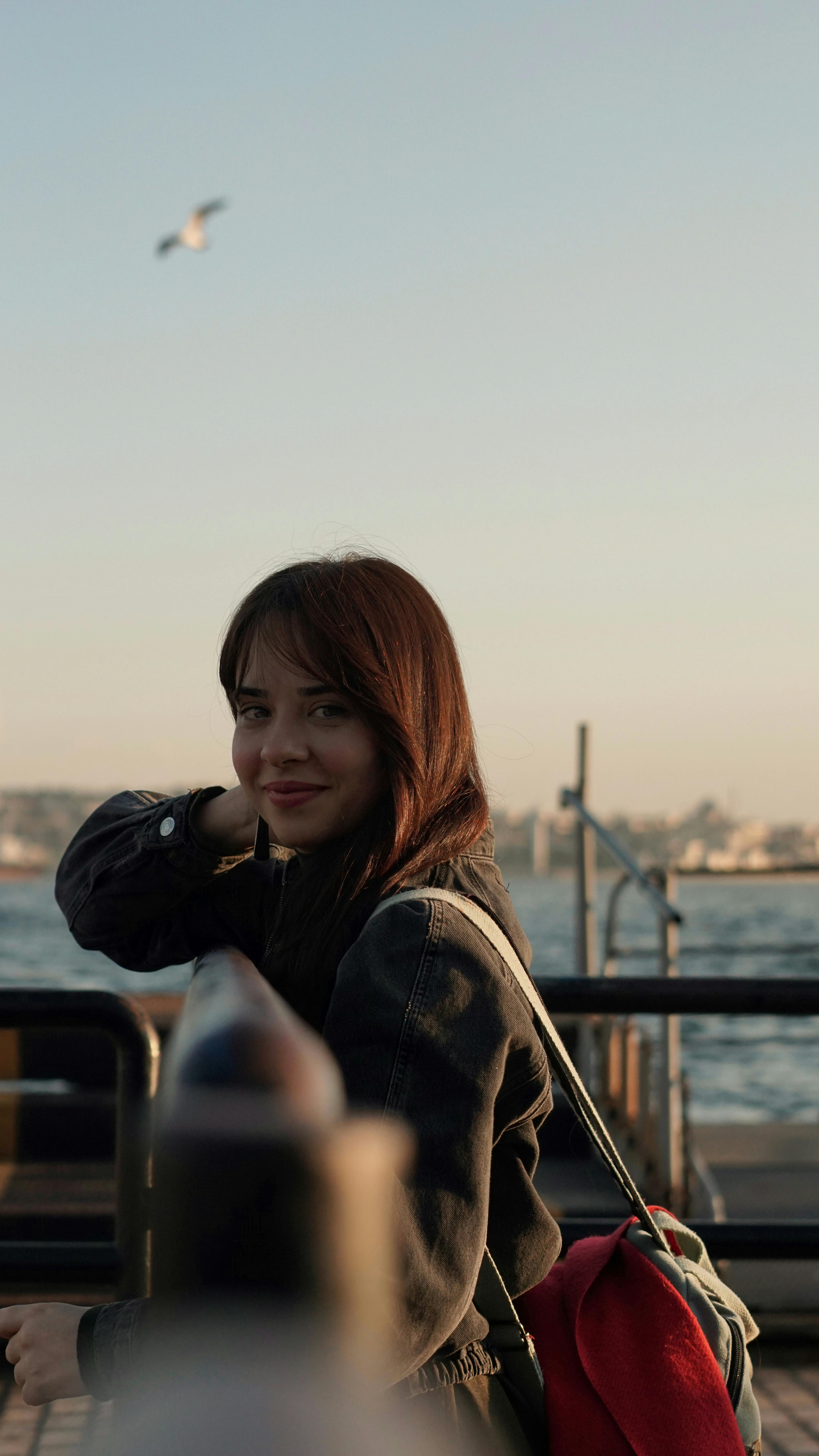 Woman with brown hair smiling outdoors by the sea during sunset.
