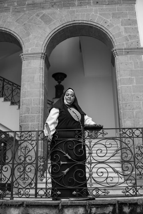A woman in a nun's habit stands on a balcony