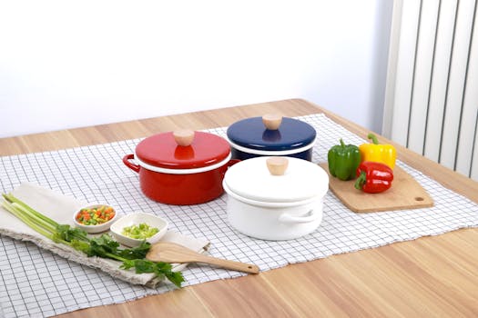 Three colorful pots with fresh vegetables and utensils on a wooden table.