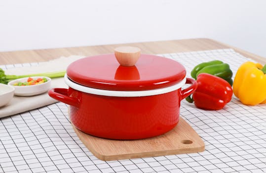 A vibrant red cooking pot with bell peppers on a checked table for a culinary setup.