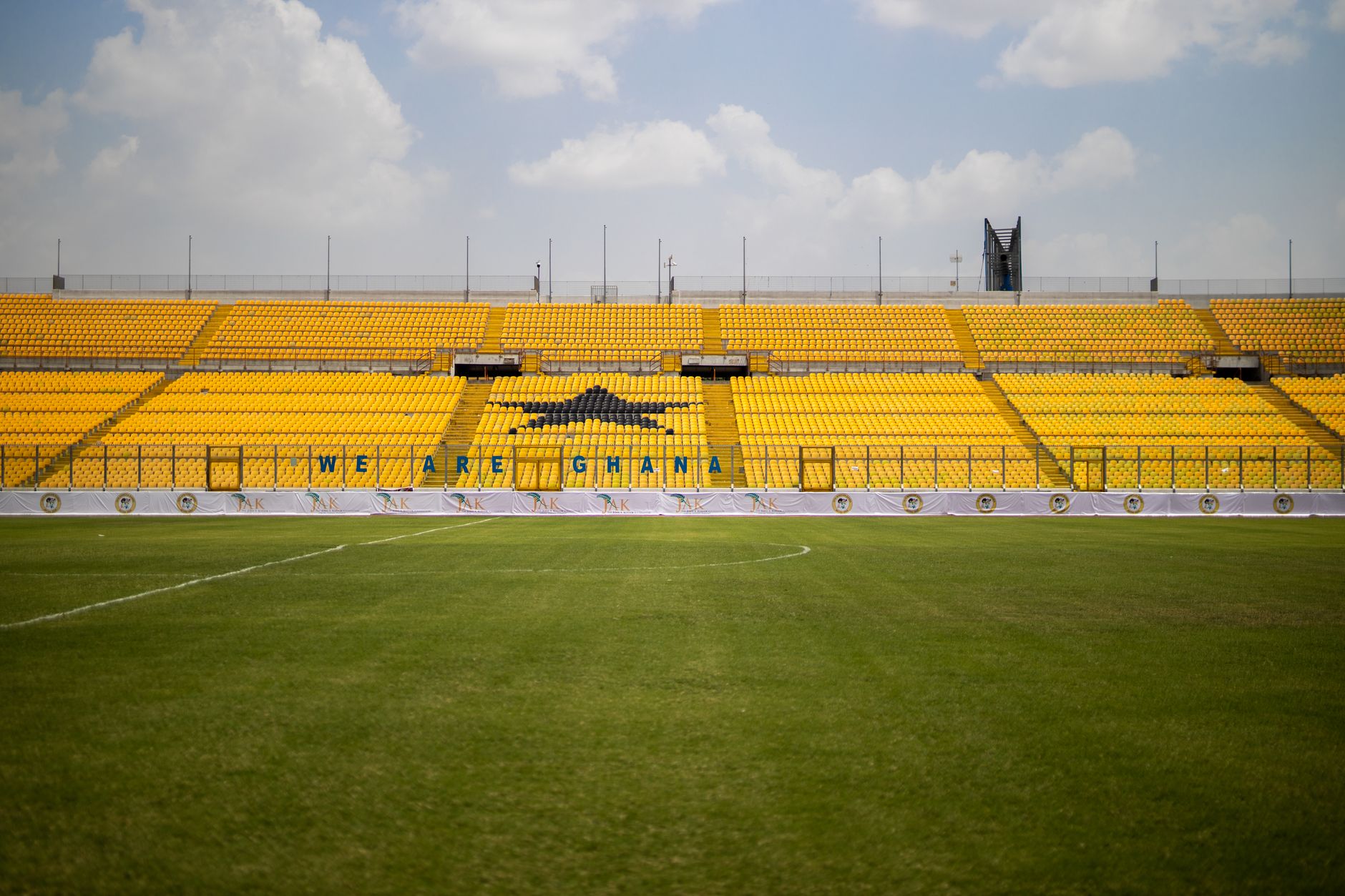 Stadium with bright yellow seats and green lawn under a blue sky in Ghana. Ideal for sports events.