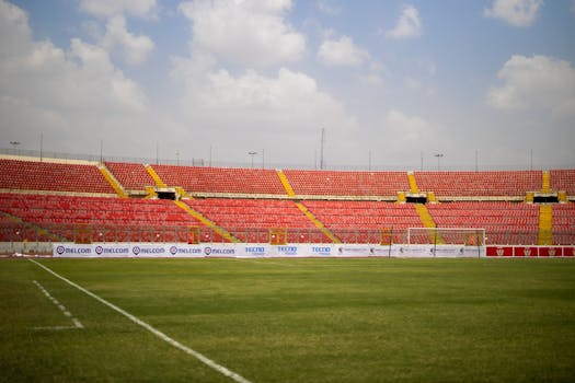 Expansive view of an empty football stadium with red seating under a cloudy sky.