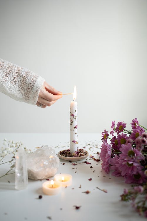 Woman Holding Her Hand near a Burning Candlestick Standing on a Table with Flowers and Crystals 