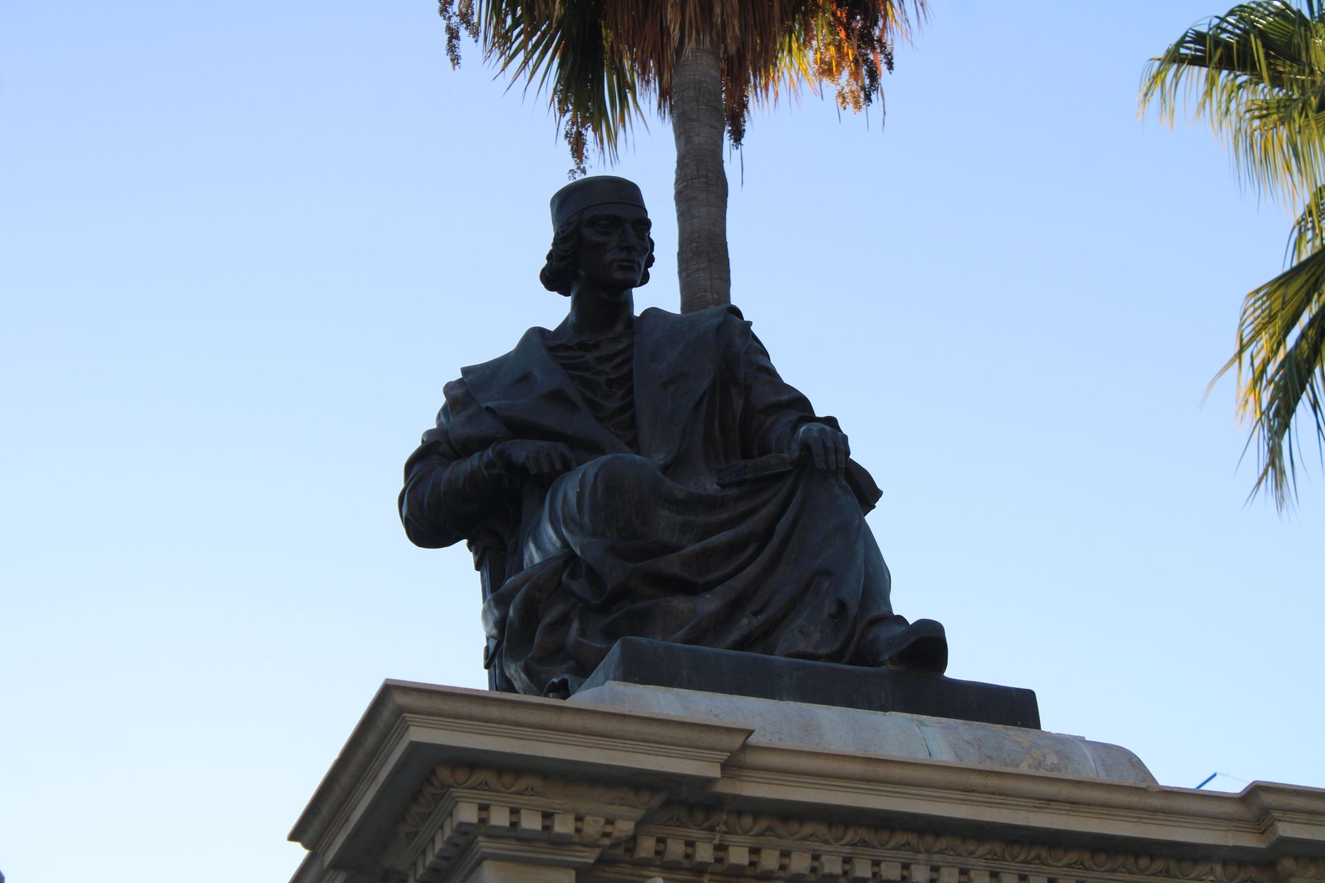 Low angle view of Elio Antonio de Nebrija monument with palm trees in Lebrija, Spain.