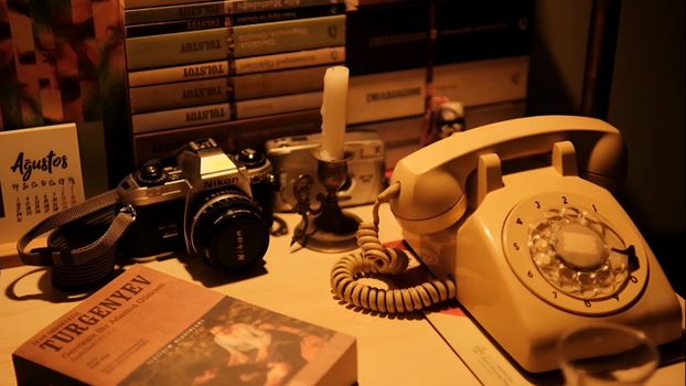 A nostalgic still life featuring a vintage telephone, camera, and classic literature on a desk.