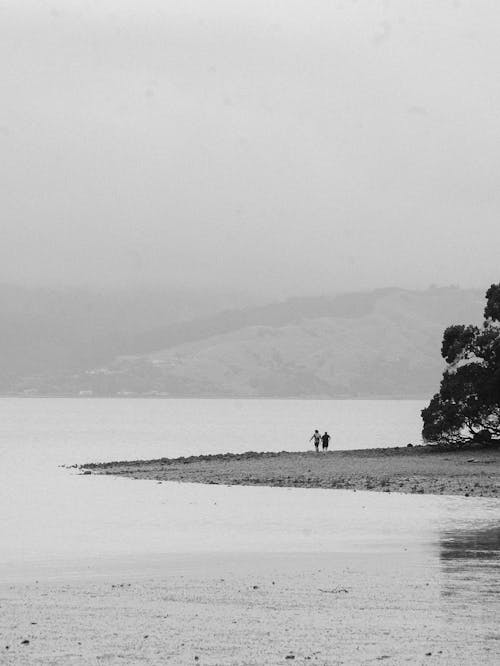 A black and white photo of two people walking on the beach