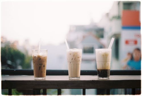 Free Three refreshing iced coffee drinks with straws on a wooden balcony railing in an urban setting. Stock Photo